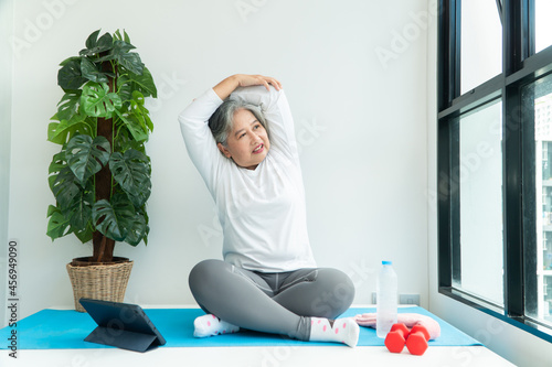 Senior Asian woman watching online courses on a laptop while exercising in the living room at home. Concept of workout training online.