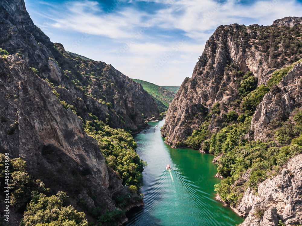 Foto Stock Drone view of Matka Canyon. Drone shot of a lake in a canyon in  North Macedonia. Rocky green slopes. Transparent water surface of the lake.  Mountain trail along the river.