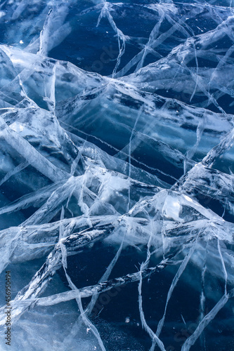Natural thick clear ice with deep cracks. Blue transparent ice with white cracks. Vertical.