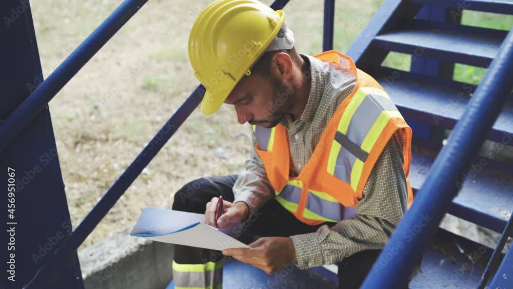 Architect in helmet and safety vest making notes in notepad Architect in helmet and safety vest making notes in notepad
