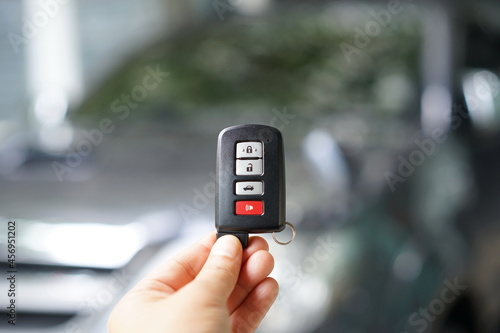 Woman holding a black remote car key. There is a small ring hanging on it and three gray buttons for locking and unlocking the car. red button for emergency Smart key systems for modern cars 