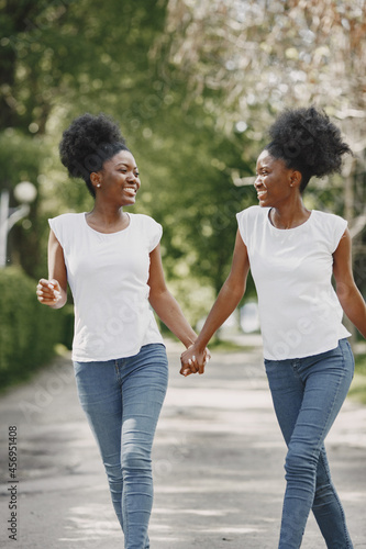 Twin afro-american sisters holding hands and walking in a park