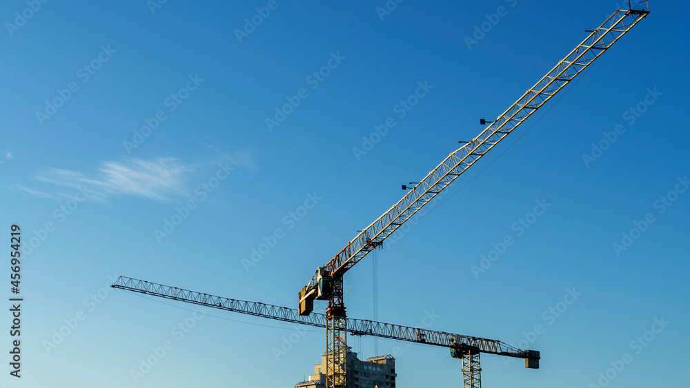 Construction site in the city centre with a couple of tall yellow cranes for lifting heavy construction material and tree on blue sky background. Construction industry. Space for text. Construction site in the city centre with a couple of tall yellow cranes for lifting heavy construction material and tree on blue sky background. Construction industry. Space for text.