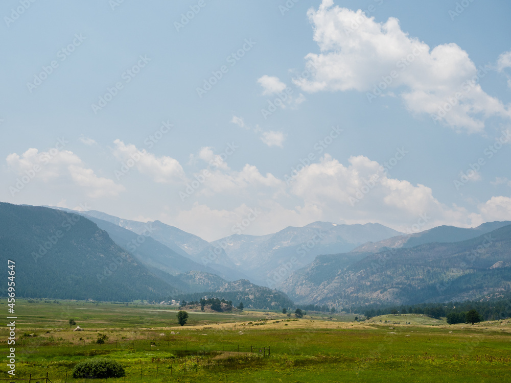 A bright green meadow with the Rocky Mountains in the background with lots of sky in view.