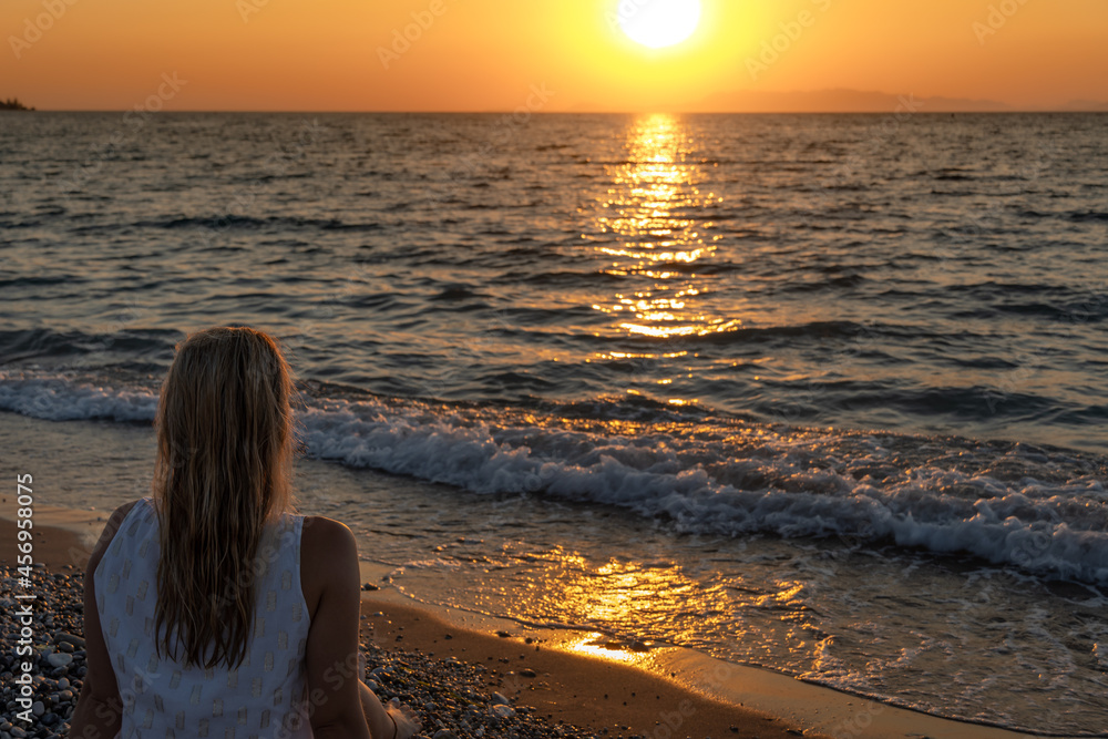 Fototapeta premium Young woman relaxing watching the waves by the sea during the sunset