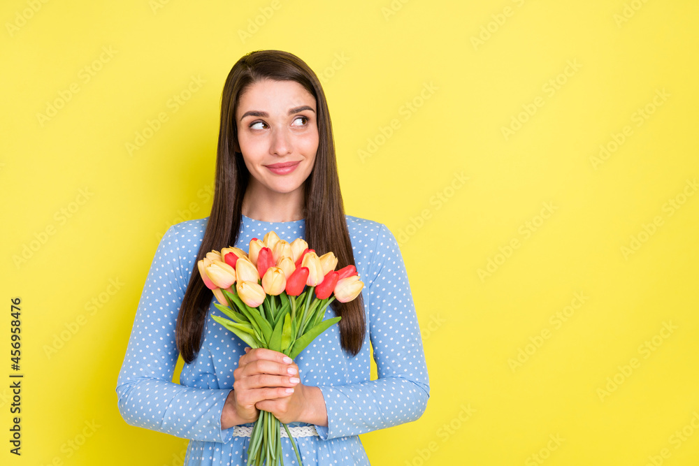Photo of pretty dreamy young lady wear dotted outfit smiling holding bunch looking empty space isolated yellow color background Photo of pretty dreamy young lady wear dotted outfit smiling holding bunch looking empty space isolated yellow color background