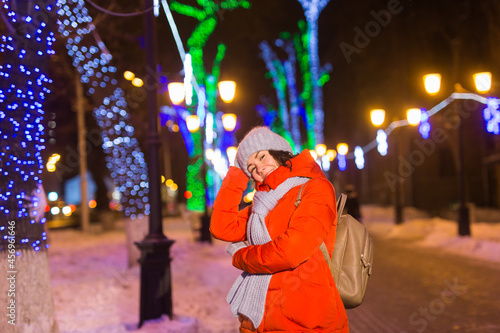 Girl having fun on christmas decoration lights street. Young happy smiling woman wearing stylish knitted scarf and jacket outdoors. Model laughing. Winter wonderland city scene  New Year party.