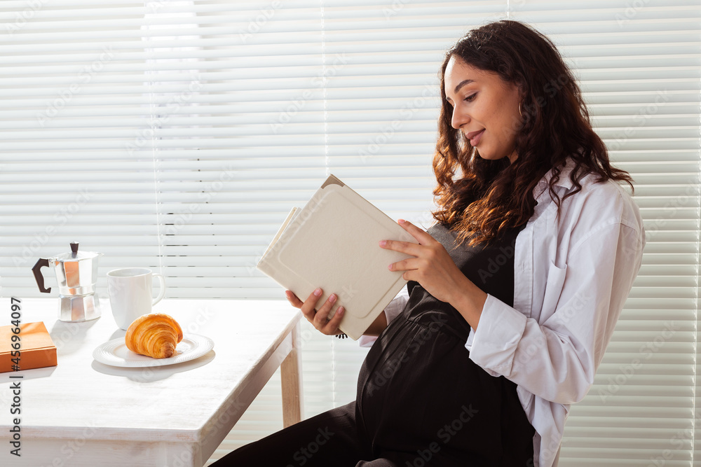 Pregnant woman is reading book while breakfast. Pregnancy and education concept Pregnant woman is reading book while breakfast. Pregnancy and education concept