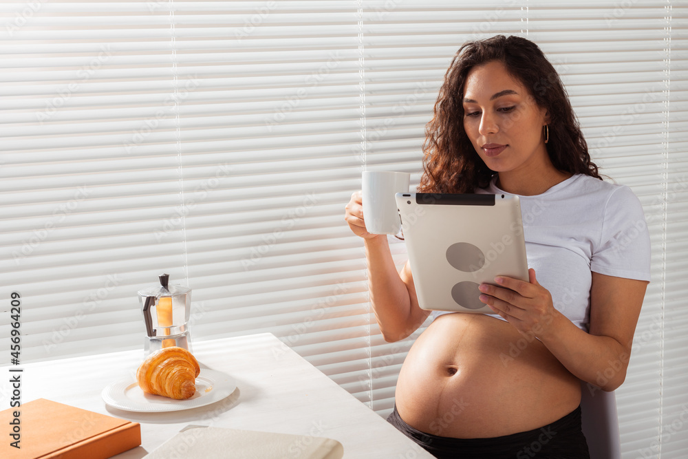 Pregnant woman using digital tablet. Breakfast time. Technology and pregnancy concept. Pregnant woman using digital tablet. Breakfast time. Technology and pregnancy concept.
