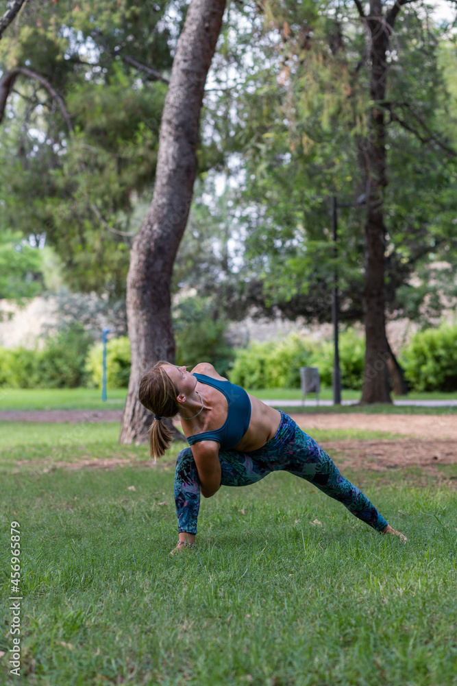 Woman stretching and performing Bound Revolved Crescent Lunge in green park Woman stretching and performing Bound Revolved Crescent Lunge in green park