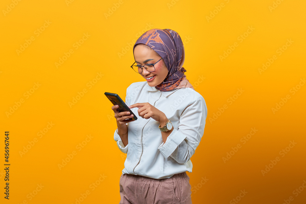Portrait of beautiful Asian woman smiling using mobile phone over yellow background Portrait of beautiful Asian woman smiling using mobile phone over yellow background