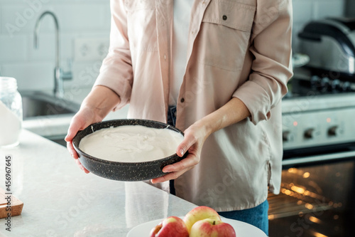 A woman in the kitchen holds a baking dish with a dough for making a pie with apples. Cooking food. Baking from rice flour