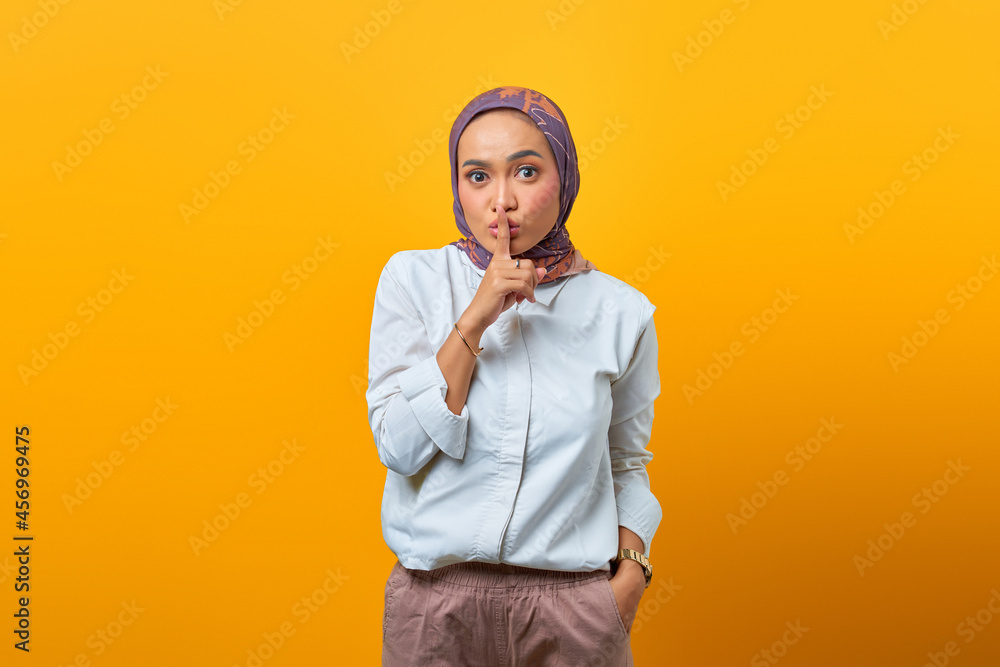 Beautiful Asian woman making finger on lips mouth silent quiet gesture over yellow background Beautiful Asian woman making finger on lips mouth silent quiet gesture over yellow background