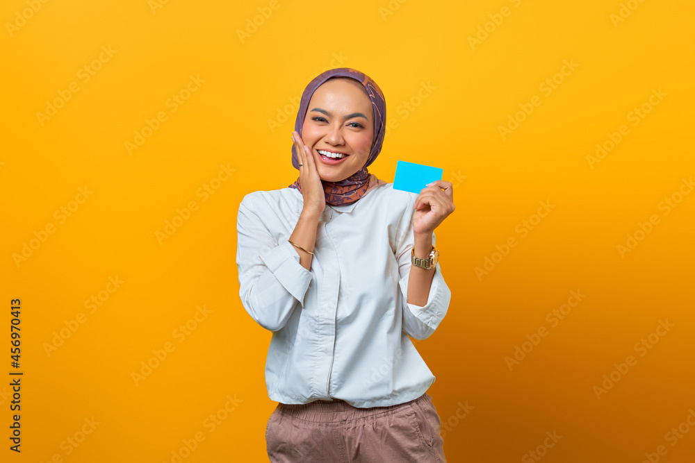 Smiling Asian woman holding blank card and touch her cheeks over yellow background Smiling Asian woman holding blank card and touch her cheeks over yellow background