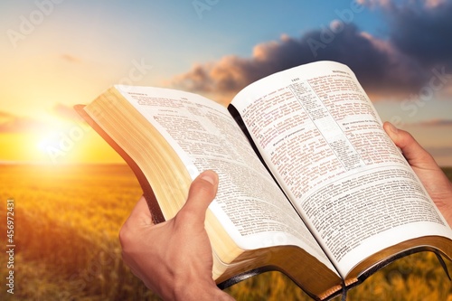 Christian human praying on the holy bible in a barley field on summer. photo