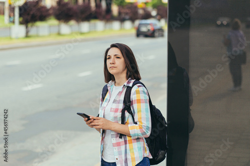 Young woman trying to catch a taxi at a bus stop using an app from a mobile phone