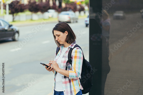 Young woman trying to catch a taxi at a bus stop using an app from a mobile phone