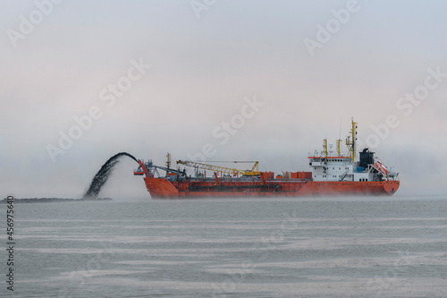 Vessel engaged in dredging at sunset time. Hopper dredger working at sea. Ship excavating material from a water environment. photo