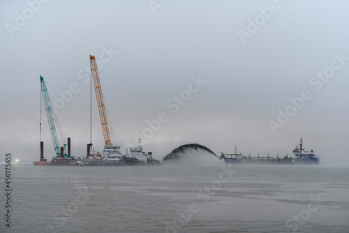 Vessel engaged in dredging at sunset time. Hopper dredger working at sea. Ship excavating material from a water environment. photo