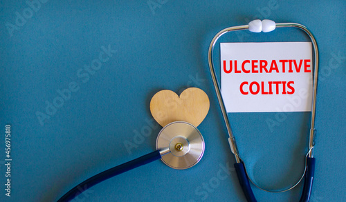 Ulcerative colitis symbol. White card with words Ulcerative colitis, beautiful blue background, wooden heart and stethoscope. Medical and ulcerative colitis concept.
