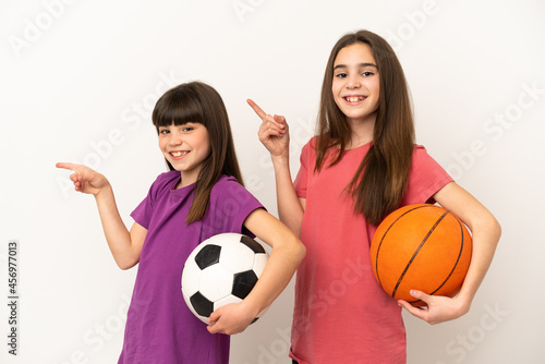 Little sisters playing football and basketball isolated on white background pointing finger to the side in lateral position