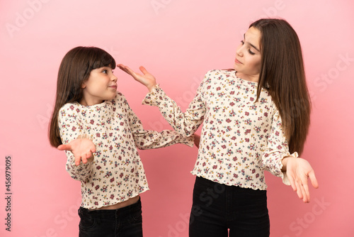 Little sisters girls isolated on pink background making unimportant gesture while lifting the shoulders