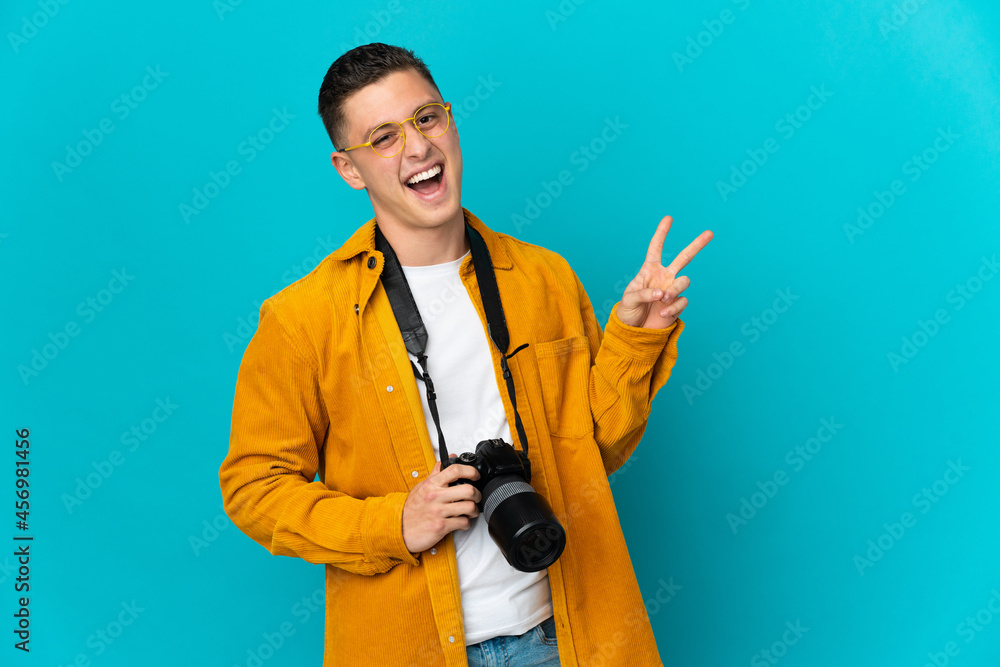 Young caucasian photographer man isolated on blue background smiling and showing victory sign Young caucasian photographer man isolated on blue background smiling and showing victory sign