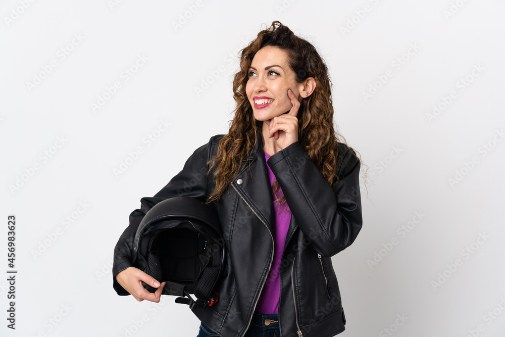 Young caucasian woman holding a motorcycle helmet thinking an idea while looking up Young caucasian woman holding a motorcycle helmet thinking an idea while looking up