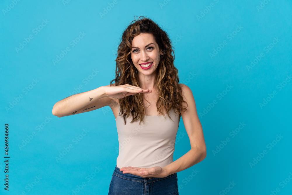 Young caucasian woman isolated on blue background holding copyspace imaginary on the palm to insert an ad Young caucasian woman isolated on blue background holding copyspace imaginary on the palm to insert an ad