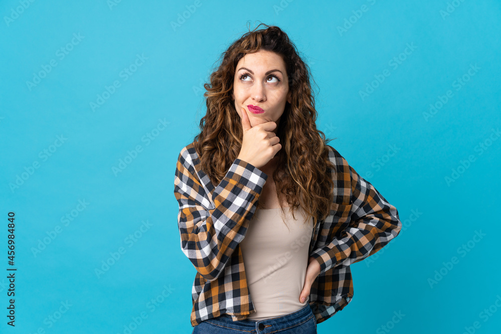 Fototapeta premium Young caucasian woman isolated on blue background having doubts and with confuse face expression