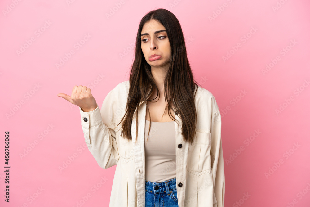 Young caucasian woman isolated on pink background unhappy and pointing to the side Young caucasian woman isolated on pink background unhappy and pointing to the side