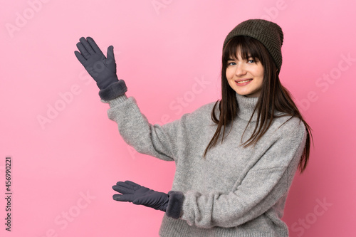 Teenager Ukrainian girl with winter hat isolated on white background extending hands to the side for inviting to come