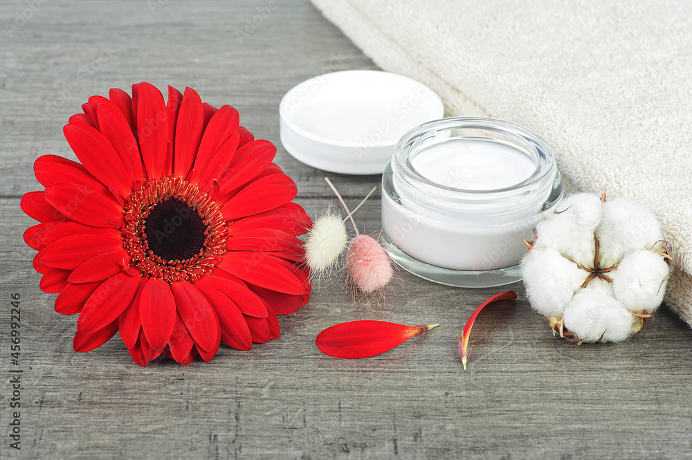 Face cream jar on wooden background with red gerbera, soft face towel and cotton flower. Face cream jar on wooden background with red gerbera, soft face towel and cotton flower.