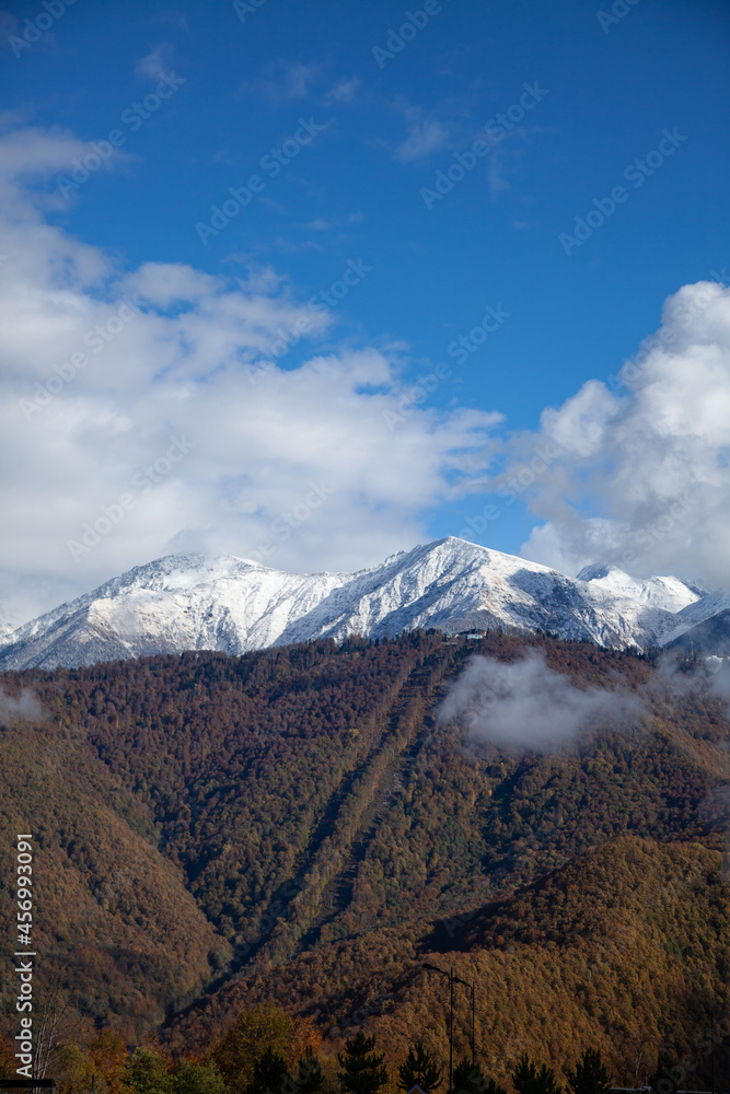 Autumn mountains with a snowy peak in blue sky