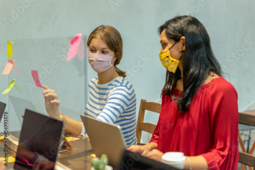 outbreak of Covid19, the new normal, people working with facemasks on laptop, small business group planning and discussing in a co working place