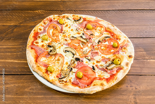 Delicious thin crust pizza with mushrooms, lots of melted cheese, flaked Parmesan cheese, pitted green olives, tomato and lots of prosciutto or ham