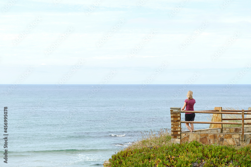 Rear view of a woman contemplating the sea from a lookout point.
