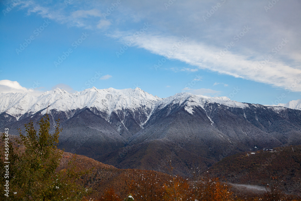 Autumn mountains with a snowy peak in blue sky