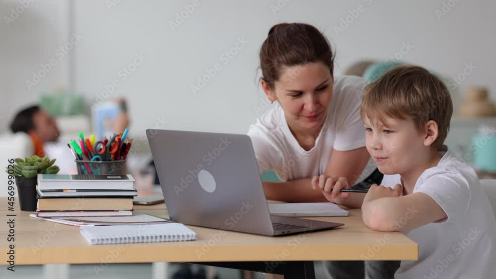 Online home school for junior schoolchildren. Spbi Positive mother helps little boy do home task at videolesson while father rests reading book on sofa Online home school for junior schoolchildren. Spbi Positive mother helps little boy do home task at videolesson while father rests reading book on sofa