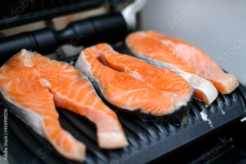 Three raw salmon steaks are toasted on a modern electric non-stick coating grill. Healthy eating concept. Close up photo with selective focus