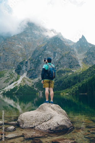 man with backpack looking at lake in mountains taking picture on phone