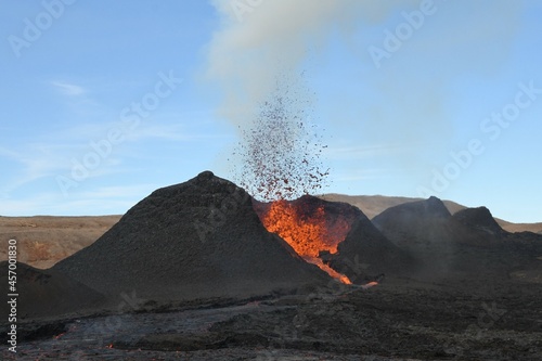 Volcanic vent at Fagradalsfjall, Iceland, erupting incandescent orange and red lava. Black cooled lava in the foreground and sky in the background. photo