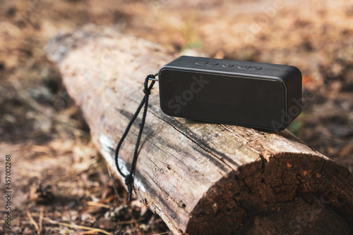Portable wireless bluetooth speaker for listening to music on a log in the forest photo