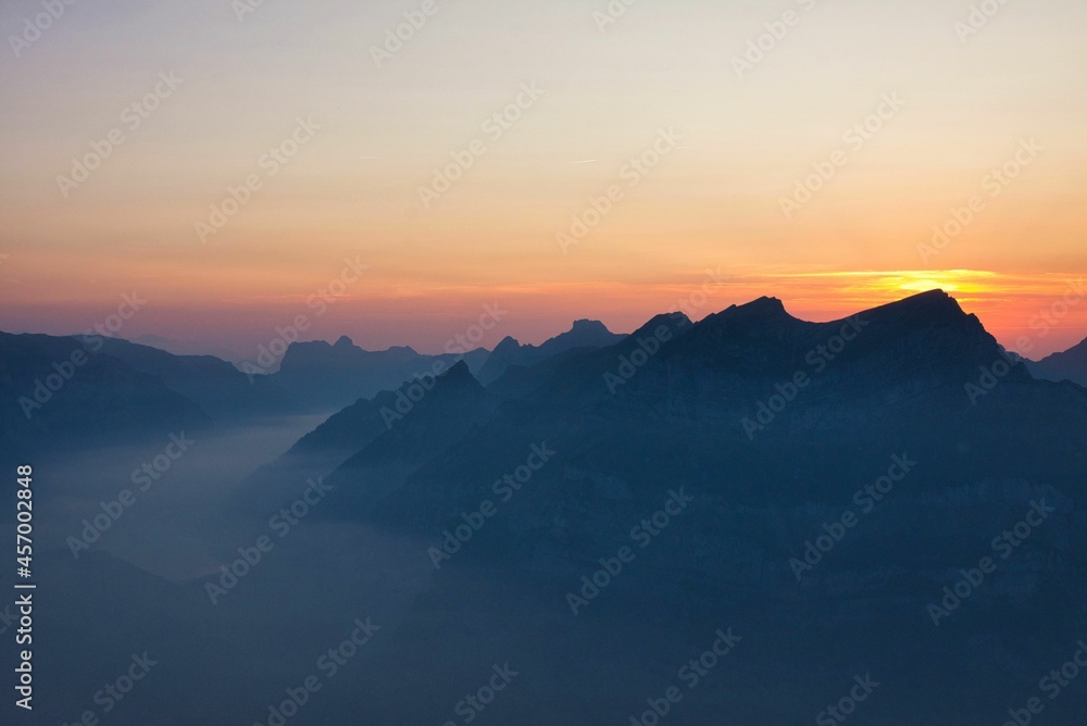 Sunbeams over Swiss mountain peaks at sunset time with valley and lake, colorful landscape picture