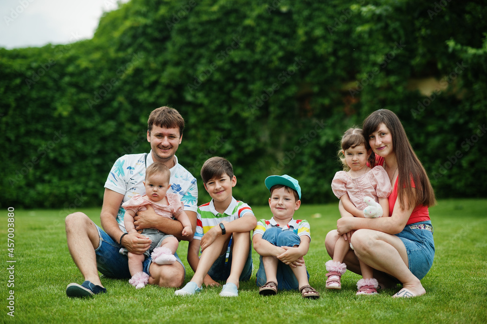 Beautiful large family with young parents and four kids sitting in green grass at courtyard. Beautiful large family with young parents and four kids sitting in green grass at courtyard.