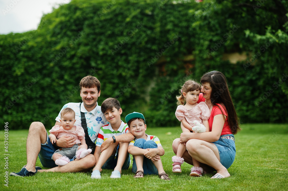 Beautiful large family with young parents and four kids sitting in green grass at courtyard. Beautiful large family with young parents and four kids sitting in green grass at courtyard.