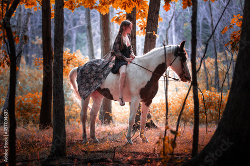 Image of a girl riding a horse in a forest during fall at sunset