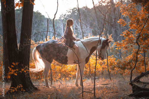 Image of a girl riding a horse in a forest during fall at sunset
