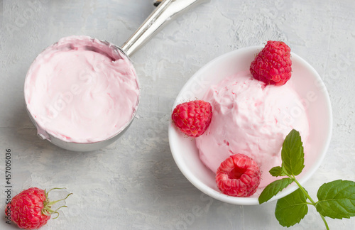Homemade raspberry ice cream in a white cup on a light background. Stainless steel spoon for ice cream balls. Fresh raspberries with mint. Delicious and romantic dessert. Top view. Top view