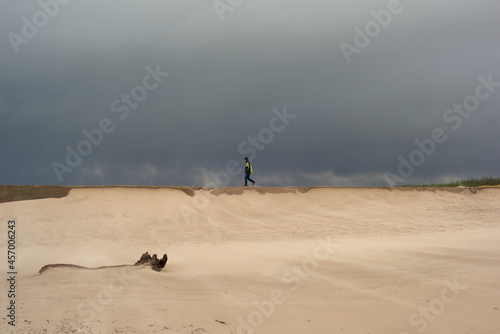 Sztorm na morzu bałtyckim, a na plaży piaskowe szaleństwo. Strumień piasku smaga po twarzy, silny wiatr unosi smugi pyłu i utrudnia spacer. Chłopiec spaceruje po falochronie. photo
